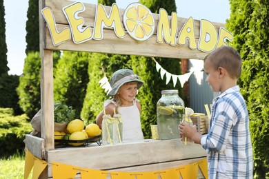 Photo of Cute little girl selling natural lemonade to boy in park