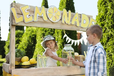 Photo of Cute little girl selling natural lemonade to boy in park