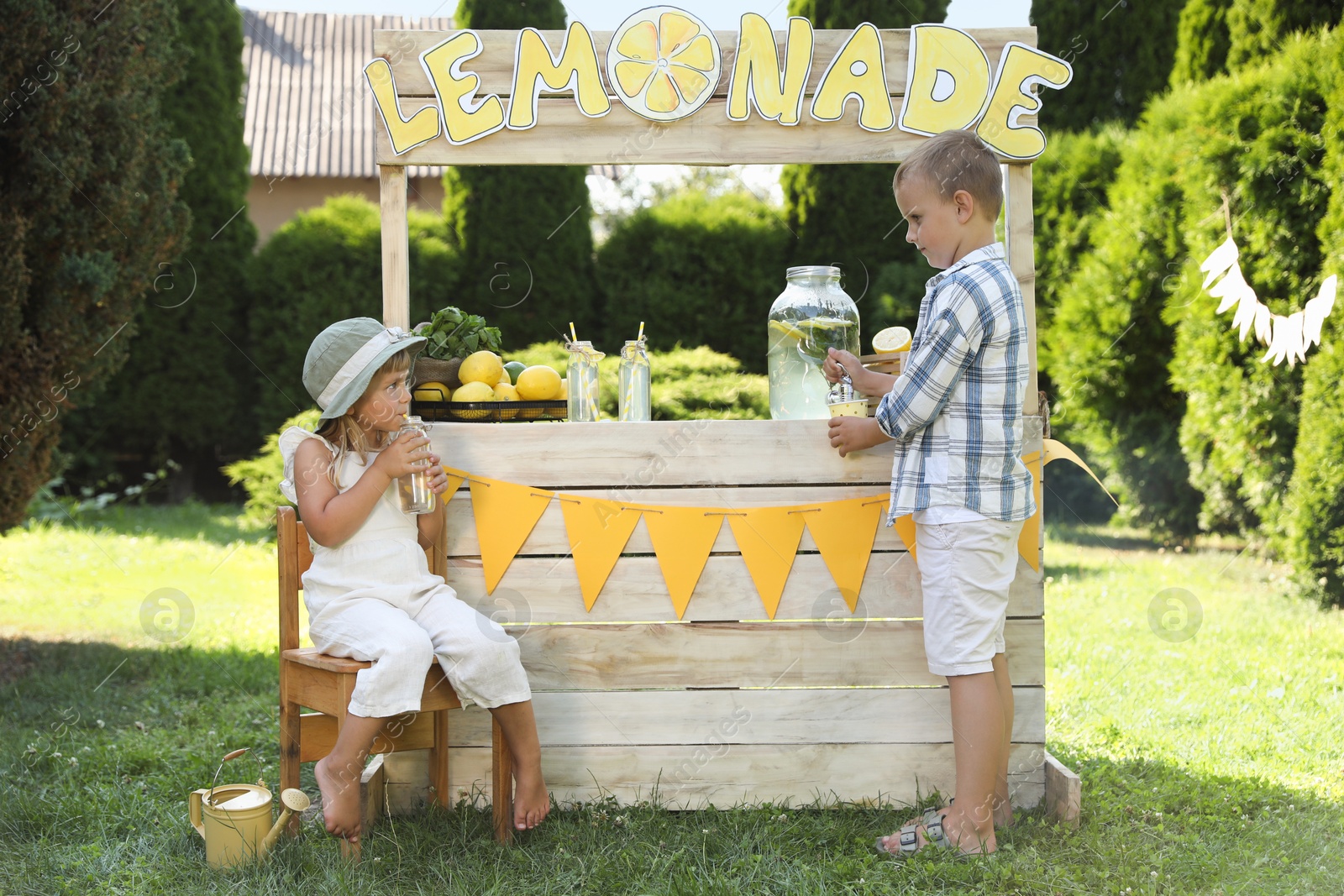 Photo of Little girl drinking beverage while boy pouring lemonade into paper cup in park