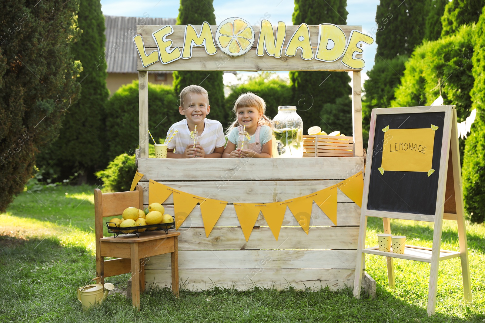 Photo of Cute little kids with refreshing drinks at lemonade stand in park