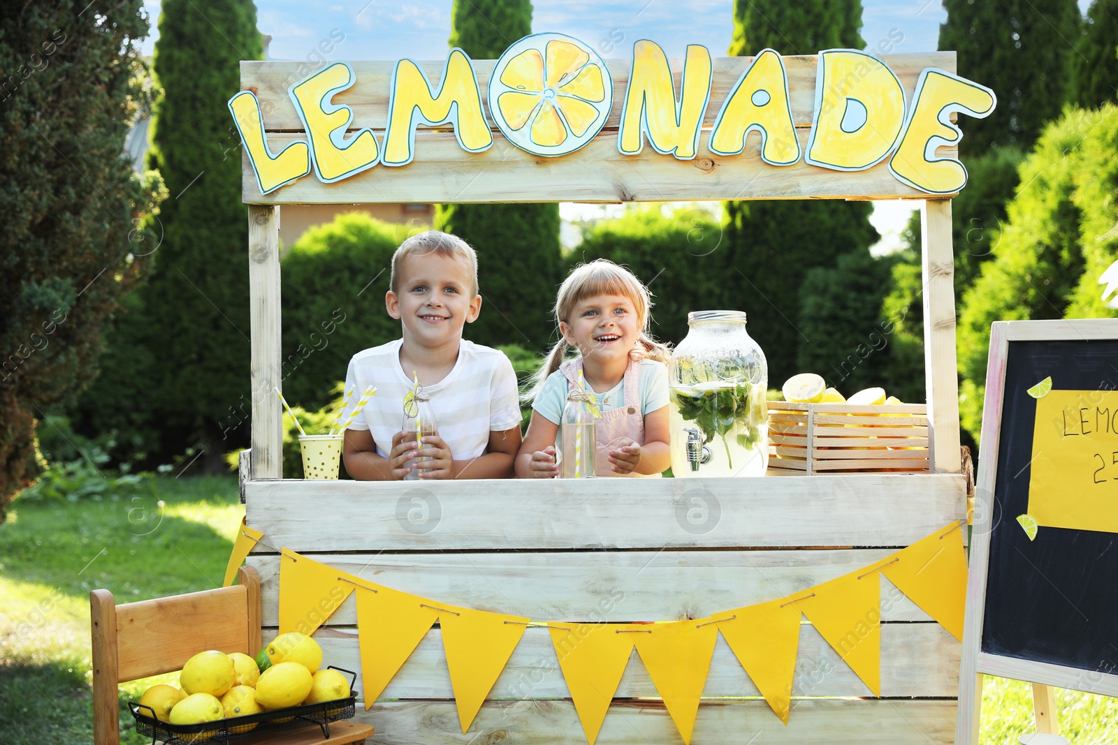 Photo of Cute little kids with refreshing drinks at lemonade stand in park