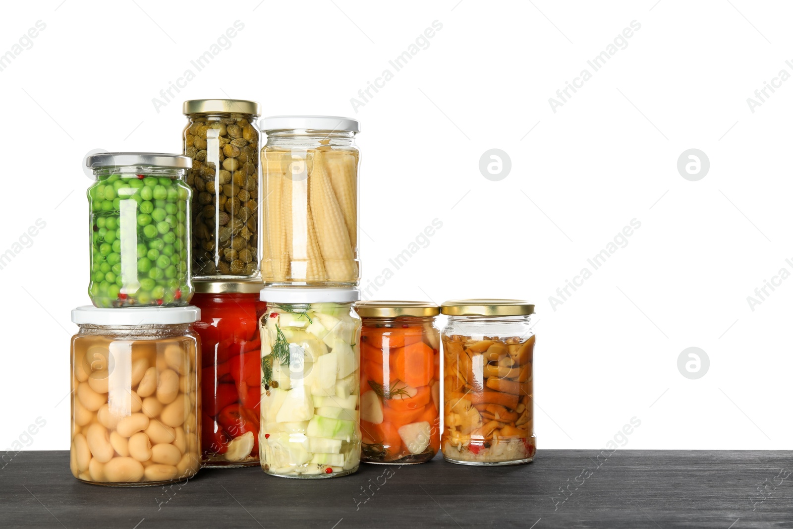 Photo of Different pickled products in jars on dark wooden table against white background. Space for text