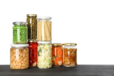 Photo of Different pickled products in jars on dark wooden table against white background. Space for text