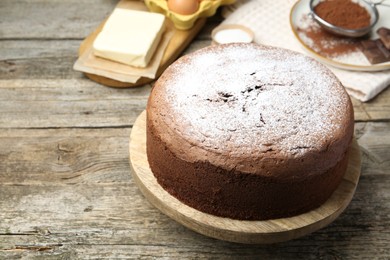 Photo of Tasty chocolate sponge cake with powdered sugar and ingredients on wooden table, closeup