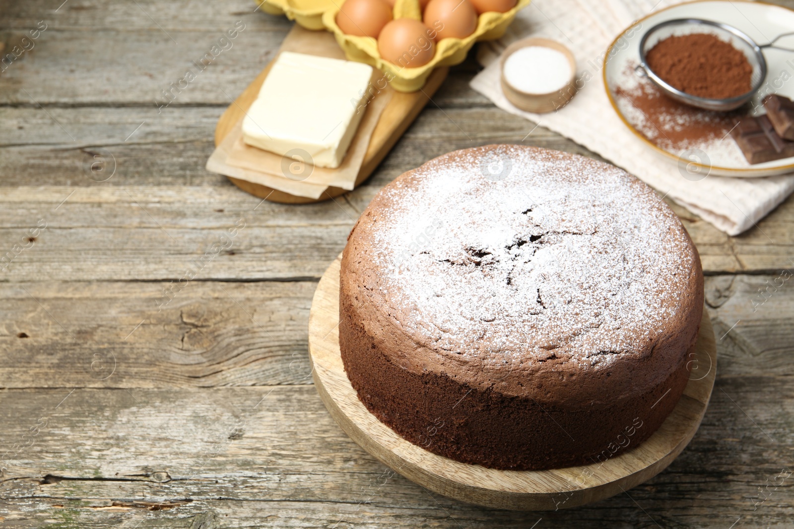 Photo of Tasty chocolate sponge cake with powdered sugar and ingredients on wooden table