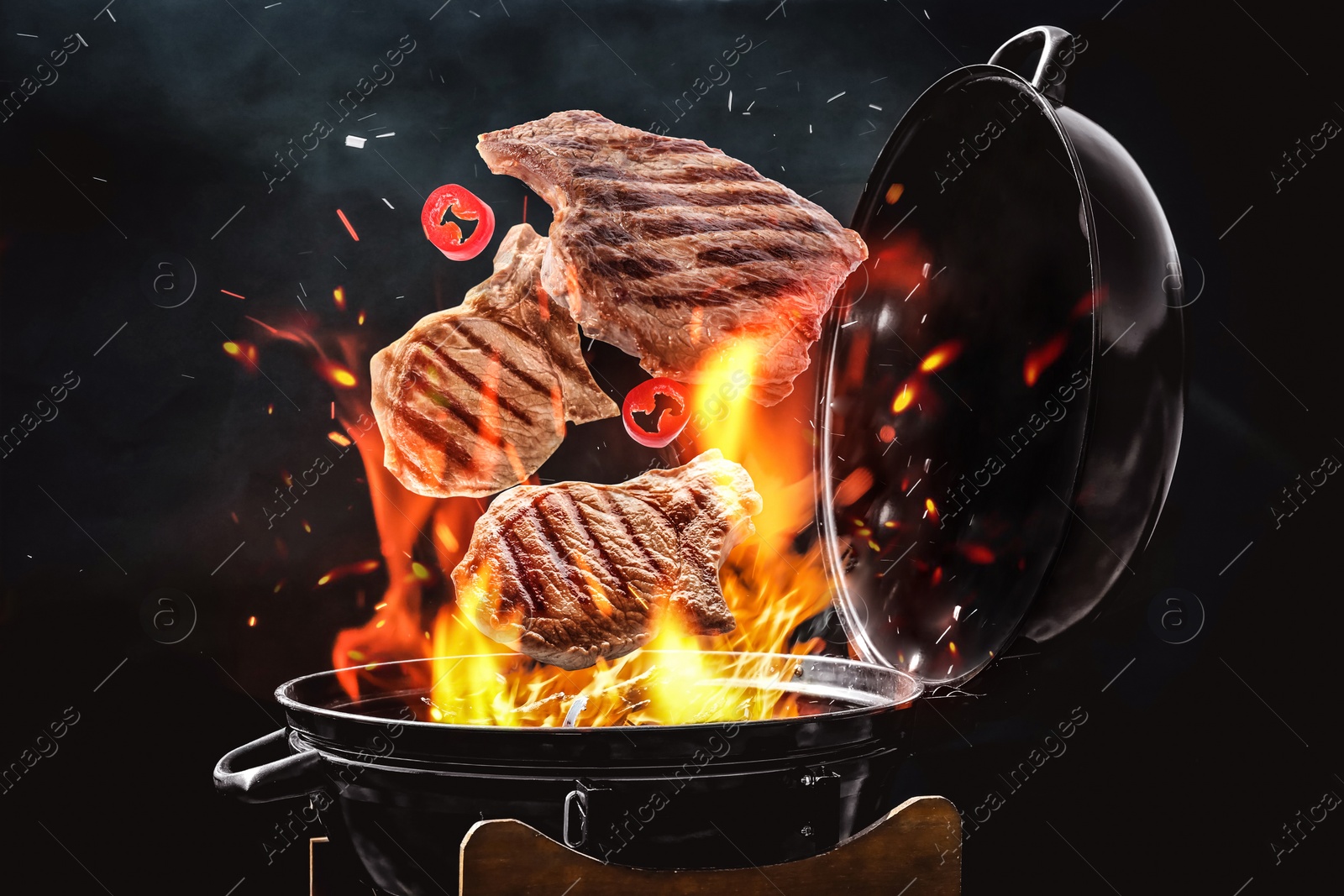 Image of Meat and chili pepper slices falling onto barbecue grill with flame against black background, closeup