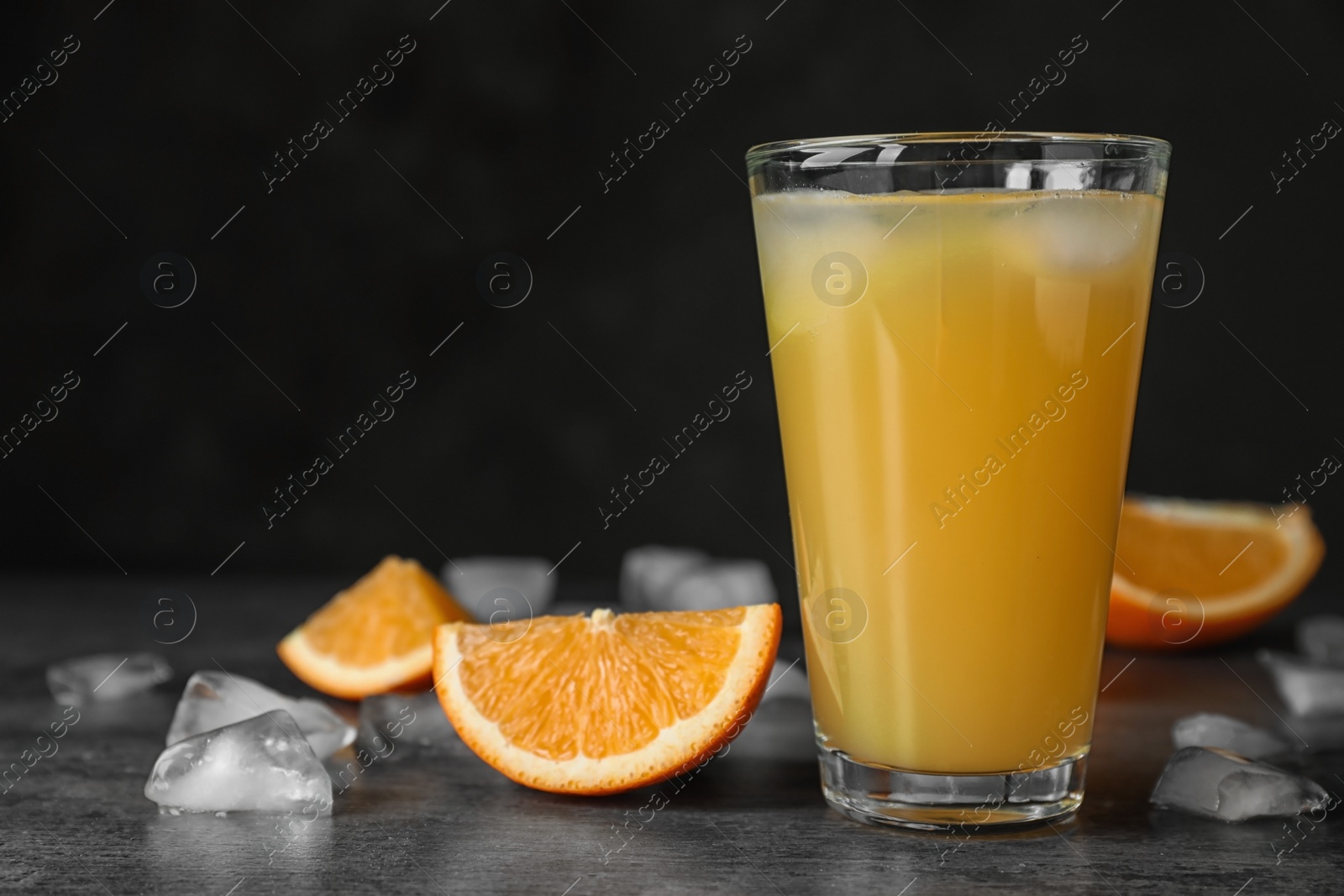 Photo of Glass of orange juice with ice cubes and cut fruit on table against black background. Space for text