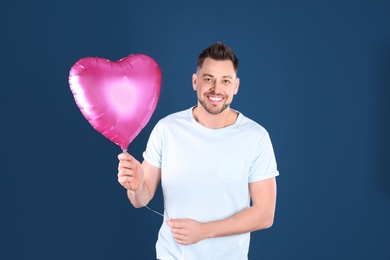 Portrait of young man with heart shaped balloon on color background