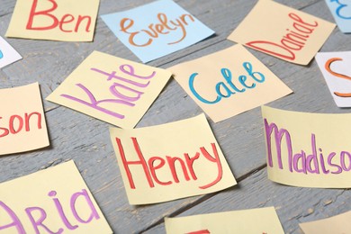 Photo of Colorful paper sheets with written different baby names on grey wooden table, closeup