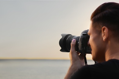 Photographer taking picture with professional camera near river, closeup