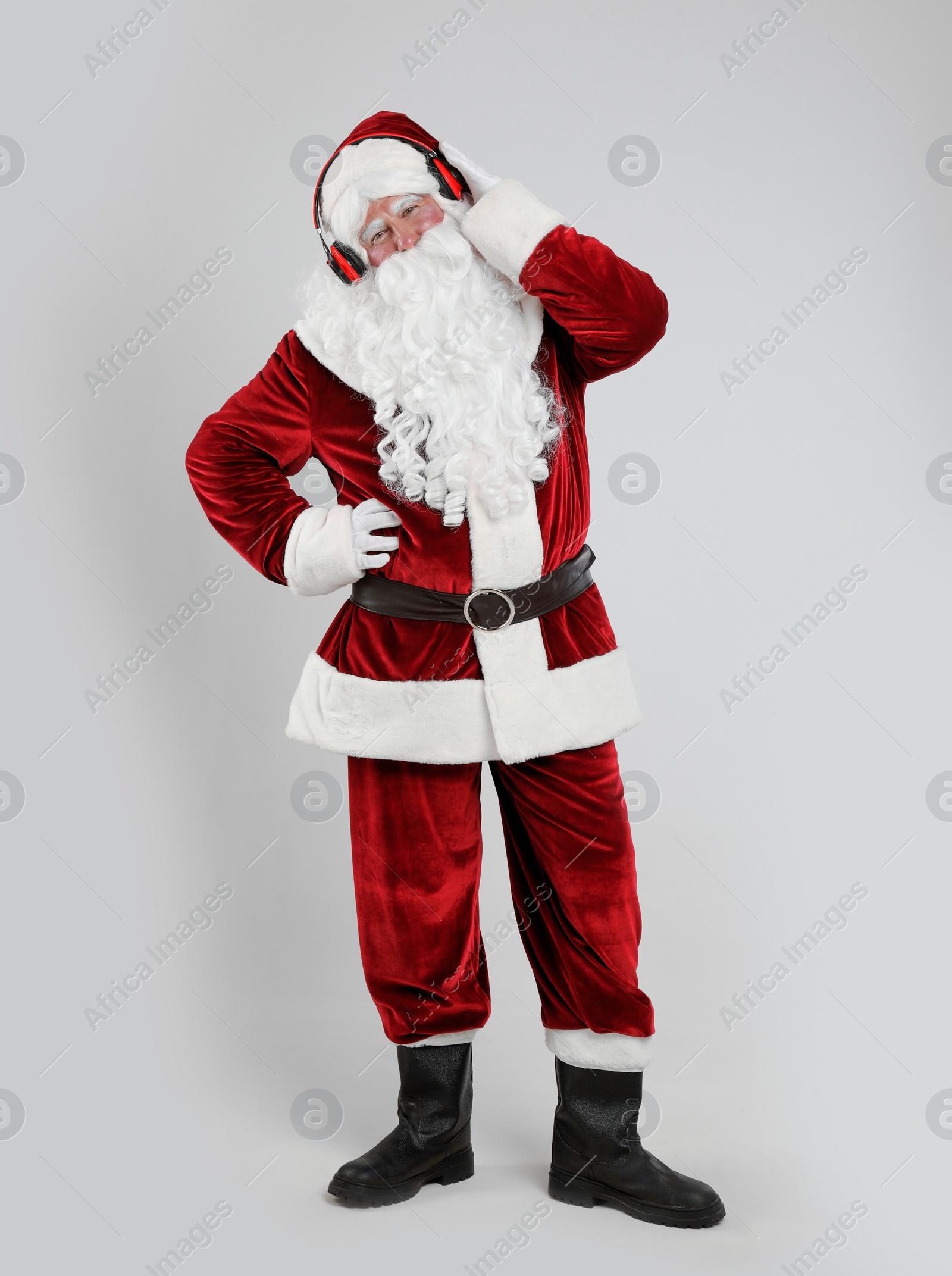 Photo of Santa Claus with headphones listening to Christmas music on light grey background