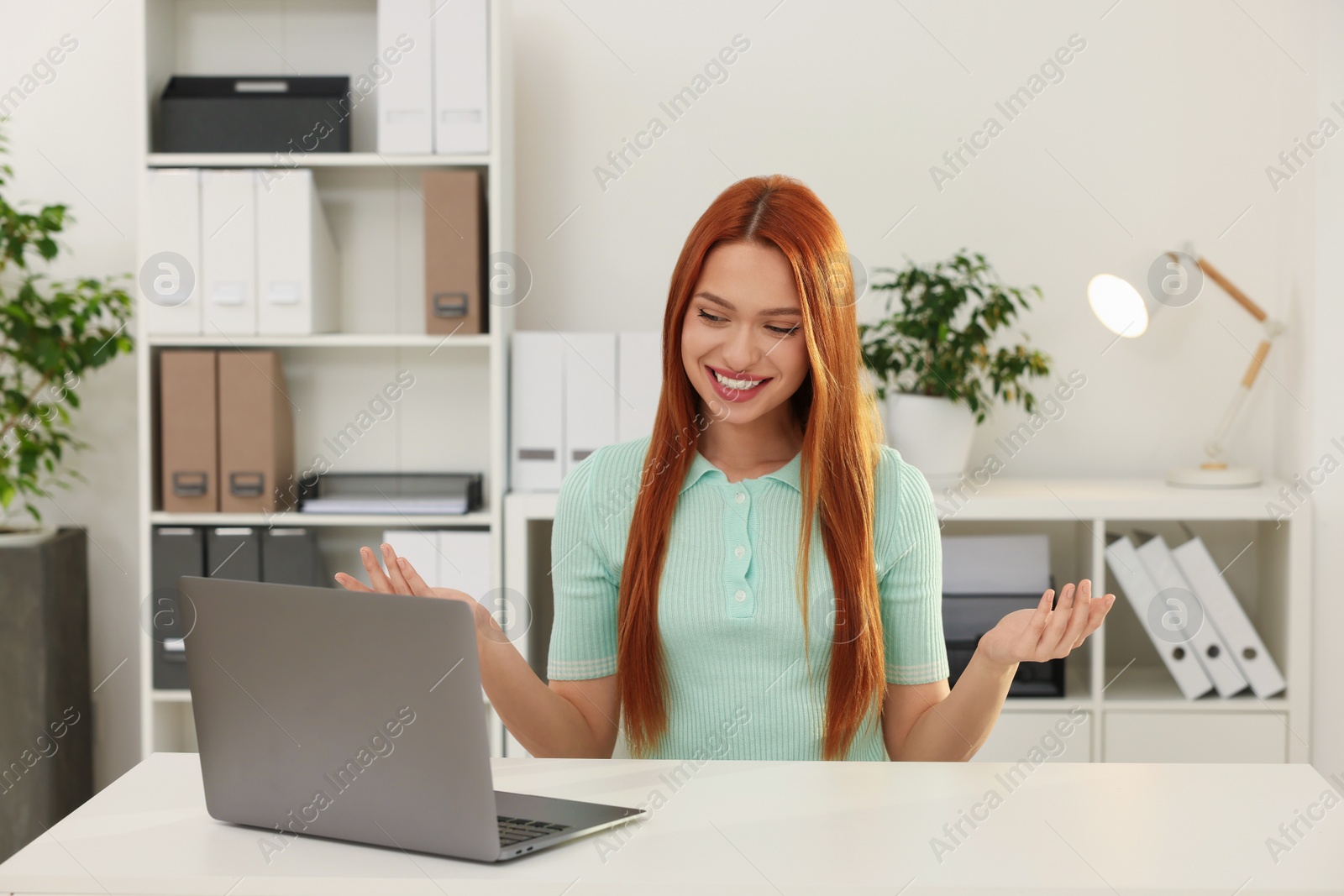 Photo of Young woman having video chat via laptop at table in office