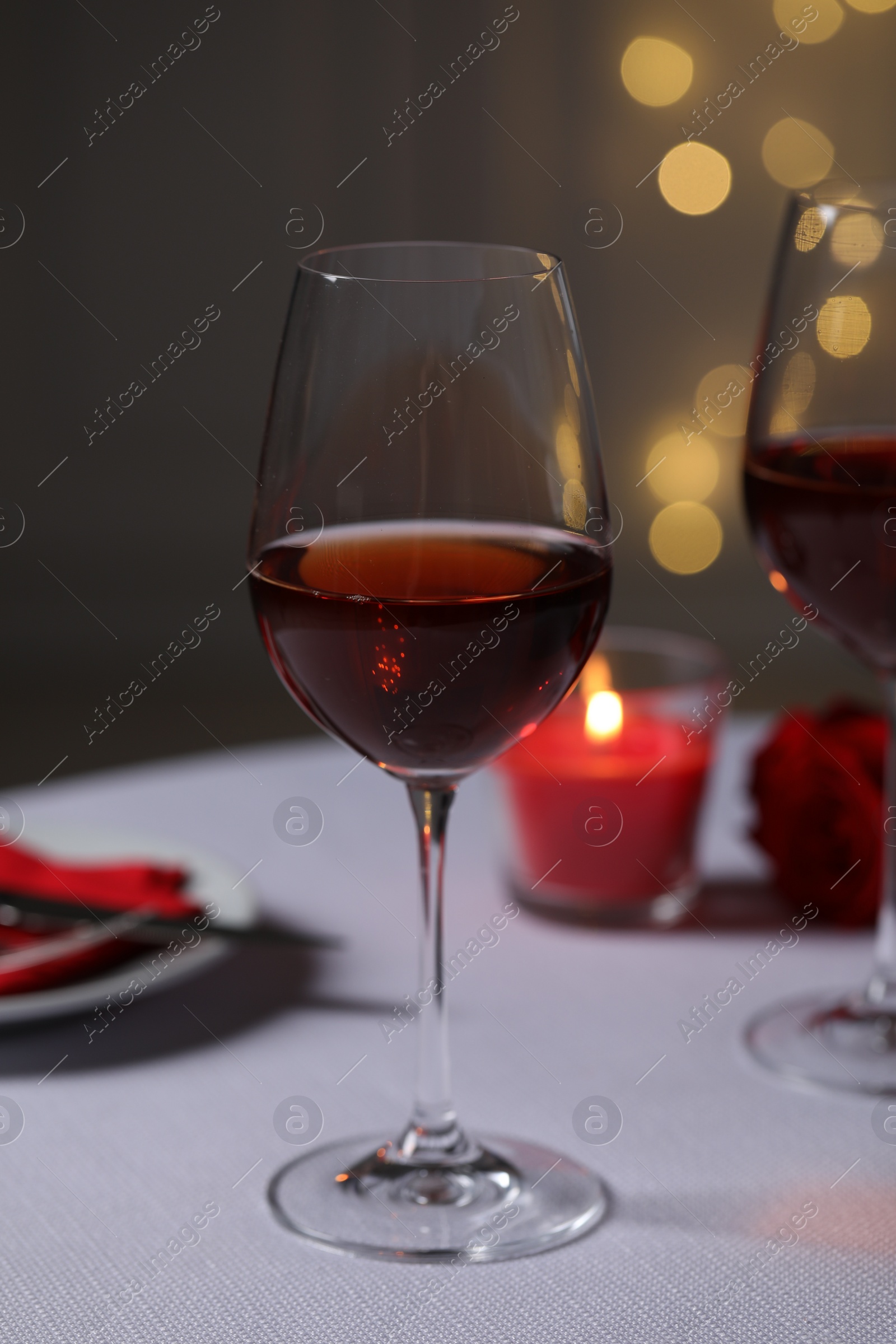 Photo of Romantic table setting with glasses of red wine, rose flower and burning candle against blurred lights