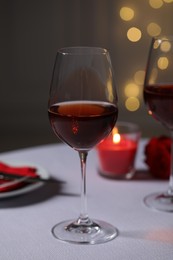 Romantic table setting with glasses of red wine, rose flower and burning candle against blurred lights