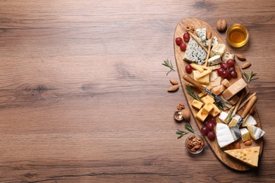 Cheese plate with honey, grapes and nuts on wooden table, flat lay. Space for text
