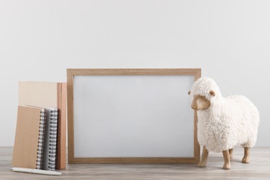 Photo of Blank photo frame, notebooks and decorative sheep on wooden table