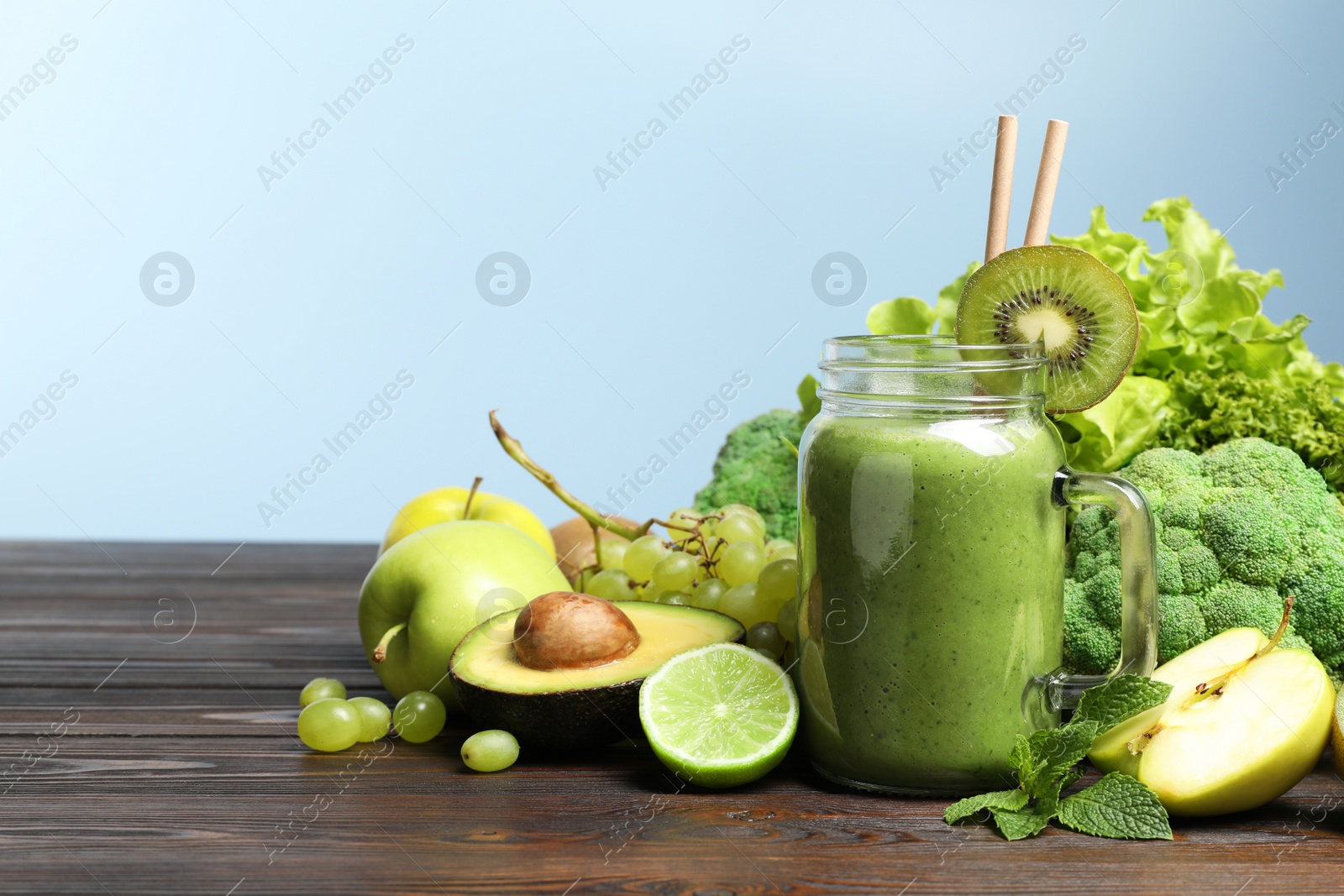 Photo of Green smoothie in mason jar and fresh ingredients on wooden table. Space for text