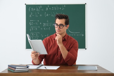 Photo of Young teacher working at table in classroom