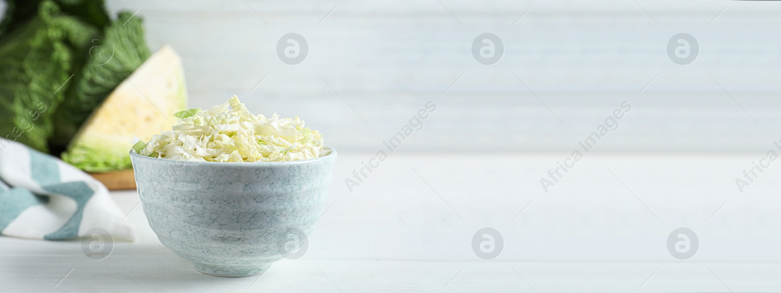 Photo of Cut fresh savoy cabbage in bowl on white wooden table. Space for text
