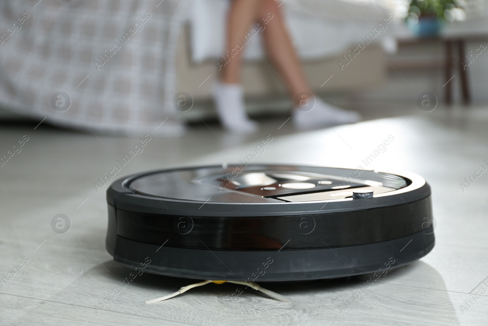 Photo of Modern robotic vacuum cleaner and blurred woman on background