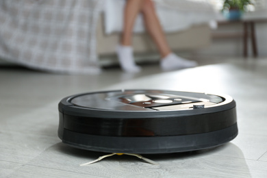 Modern robotic vacuum cleaner and blurred woman on background