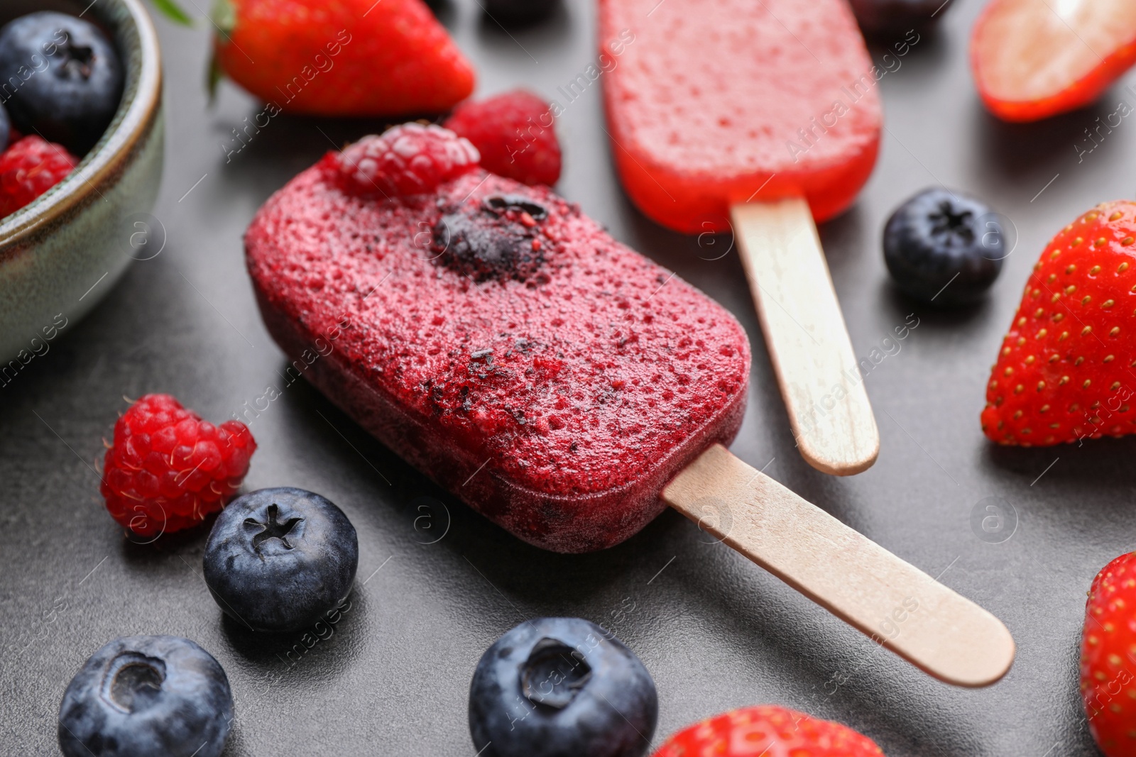 Photo of Tasty berry ice pops on dark table, closeup. Fruit popsicle