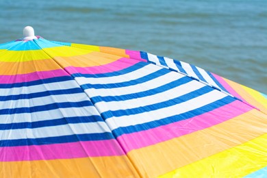Photo of Colorful striped beach umbrella near sea, closeup