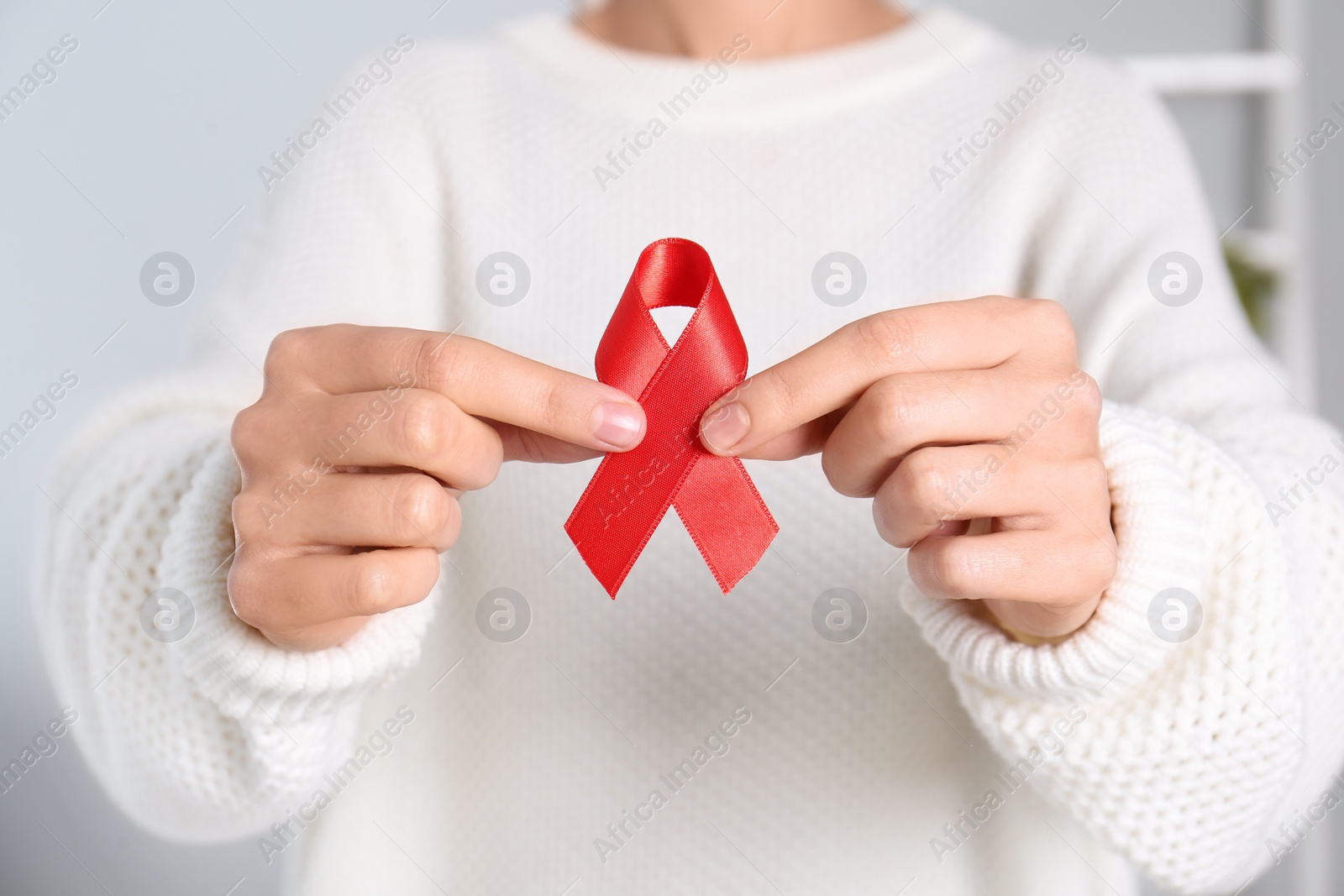 Photo of Woman holding red awareness ribbon indoors, closeup. World AIDS disease day