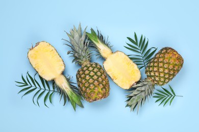 Photo of Whole and cut ripe pineapples on light blue background, flat lay