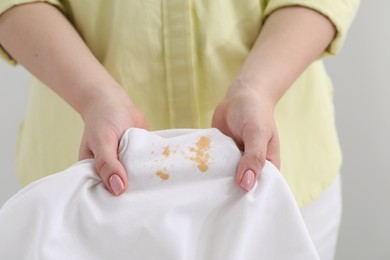 Woman holding shirt with stain against light grey background, closeup