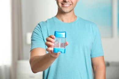 Young man holding deodorant indoors, closeup. Mockup for design