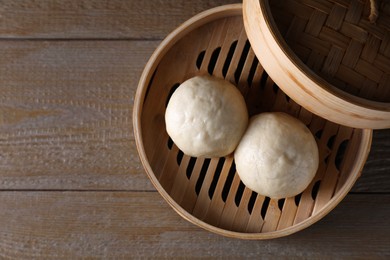 Delicious Chinese steamed buns in bamboo steamer on wooden table, top view. Space for text