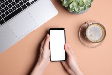 Woman using phone near laptop and cup of coffee at coral table, top view