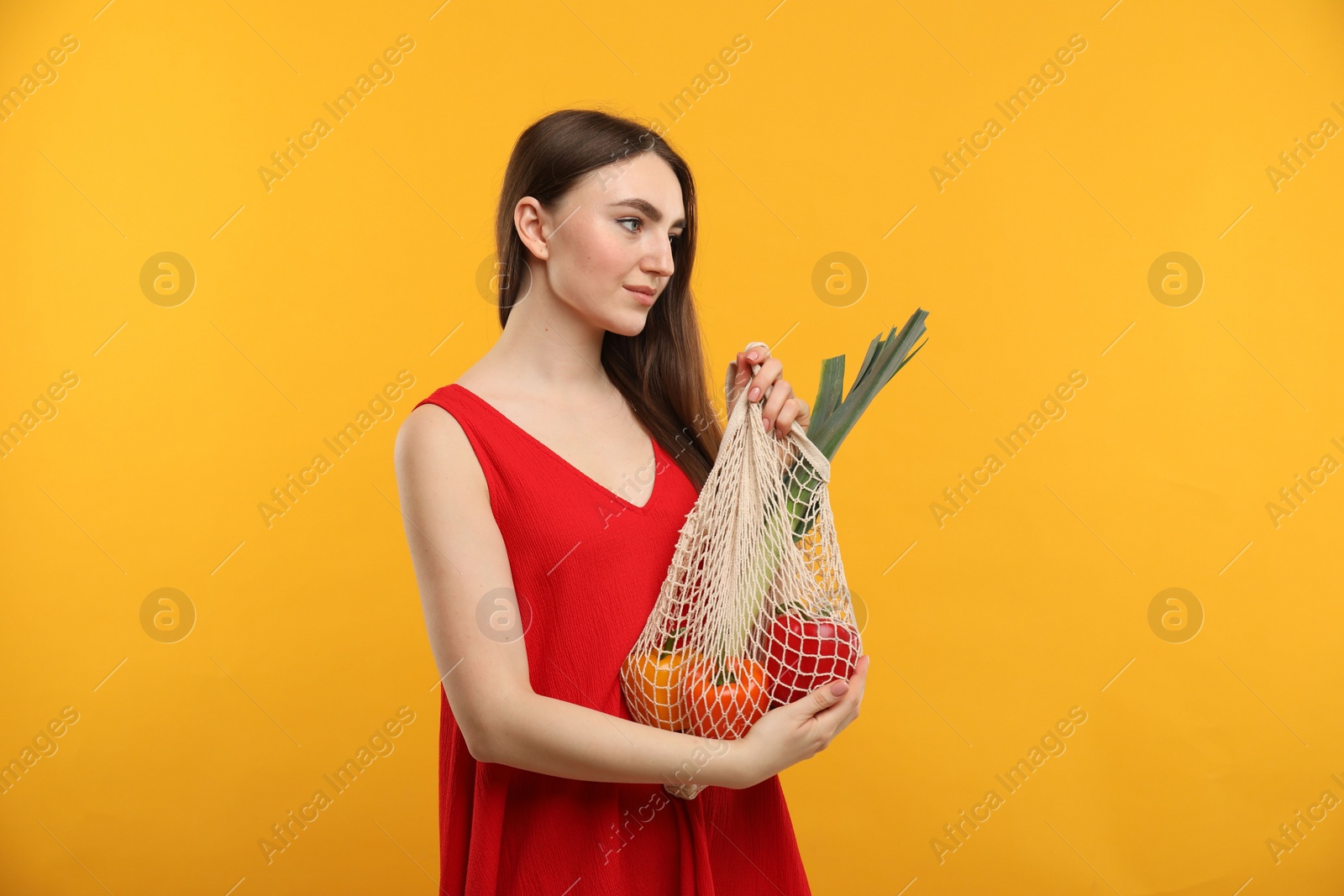 Photo of Woman with string bag of fresh vegetables on orange background