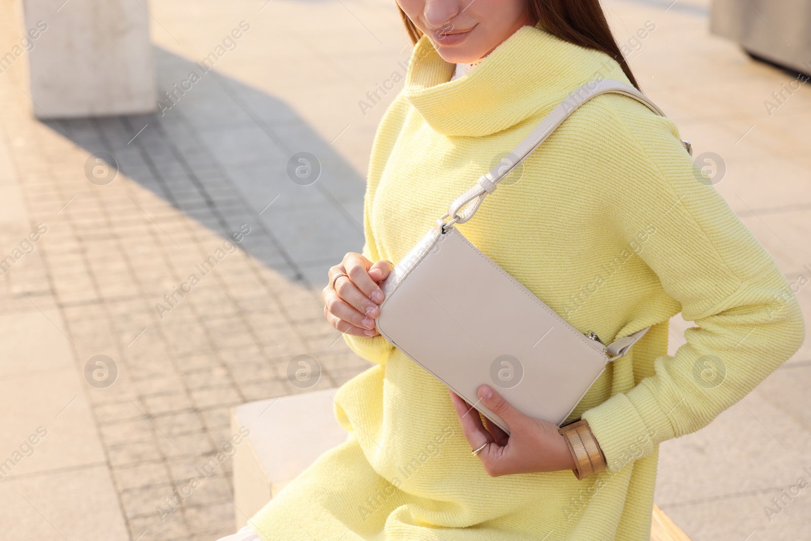 Photo of Fashionable young woman with stylish bag on bench outdoors, closeup