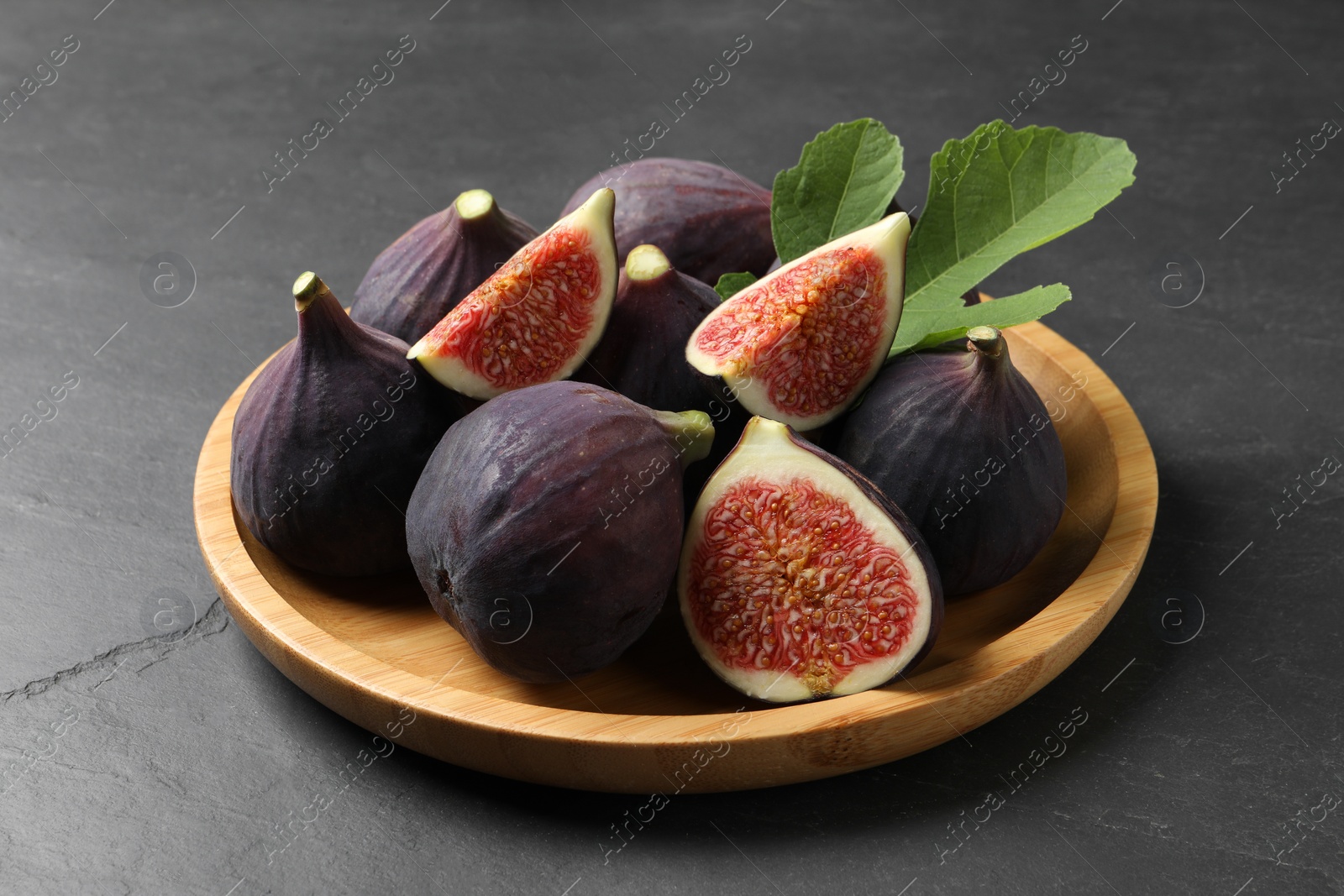 Photo of Plate with fresh ripe figs and green leaf on black table