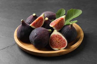 Photo of Plate with fresh ripe figs and green leaf on black table