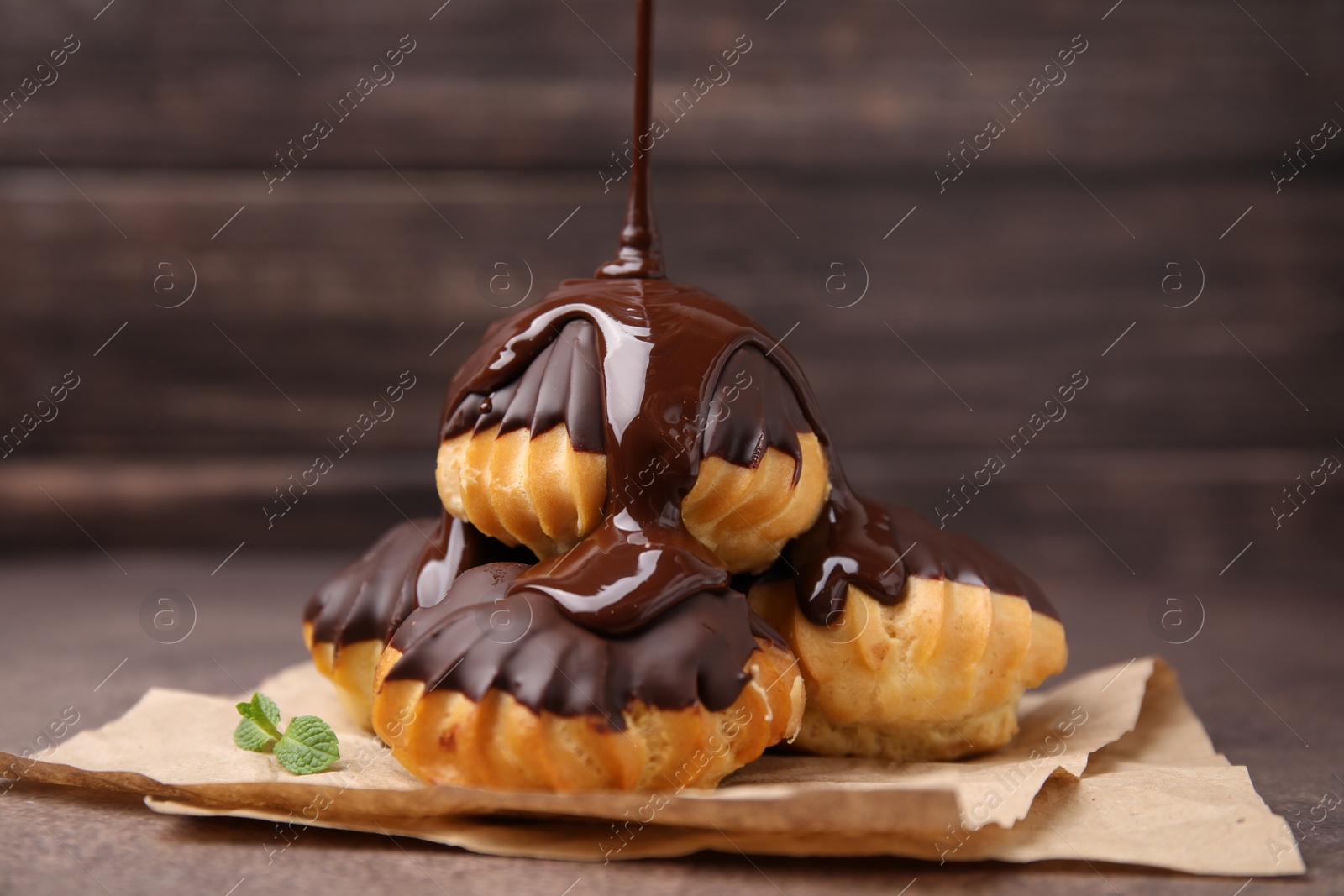 Photo of Pouring chocolate cream onto delicious profiteroles on table, closeup