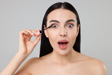 Photo of Emotional young woman applying mascara on grey background