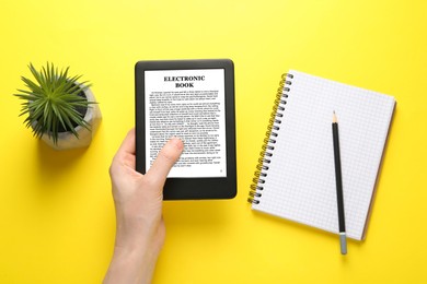 Woman using e-book reader on yellow background, top view