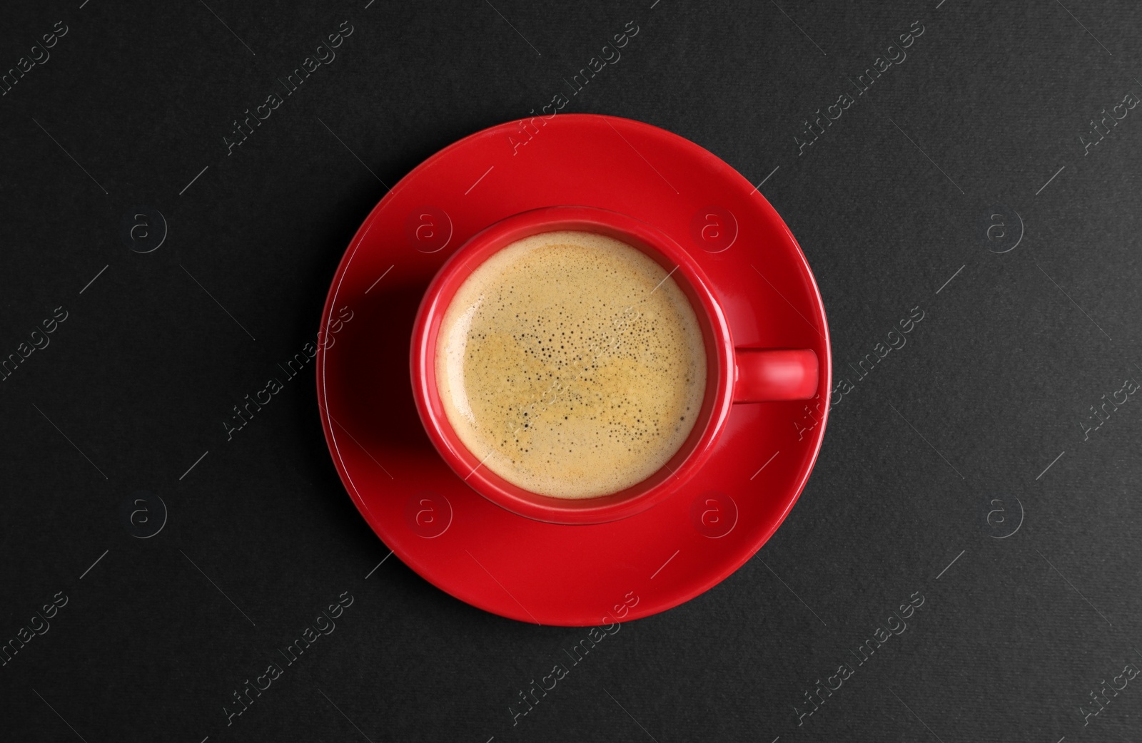 Photo of Red ceramic cup with hot aromatic coffee on black background, top view