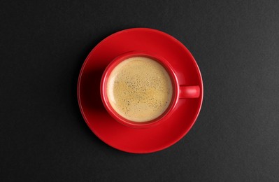 Photo of Red ceramic cup with hot aromatic coffee on black background, top view