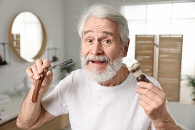 Photo of Man shaving mustache and beard with blade in bathroom