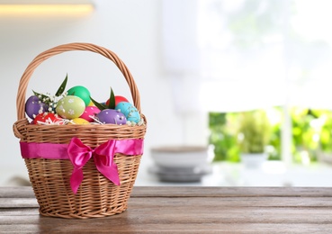 Image of Colorful Easter eggs in wicker basket on wooden table, space for text