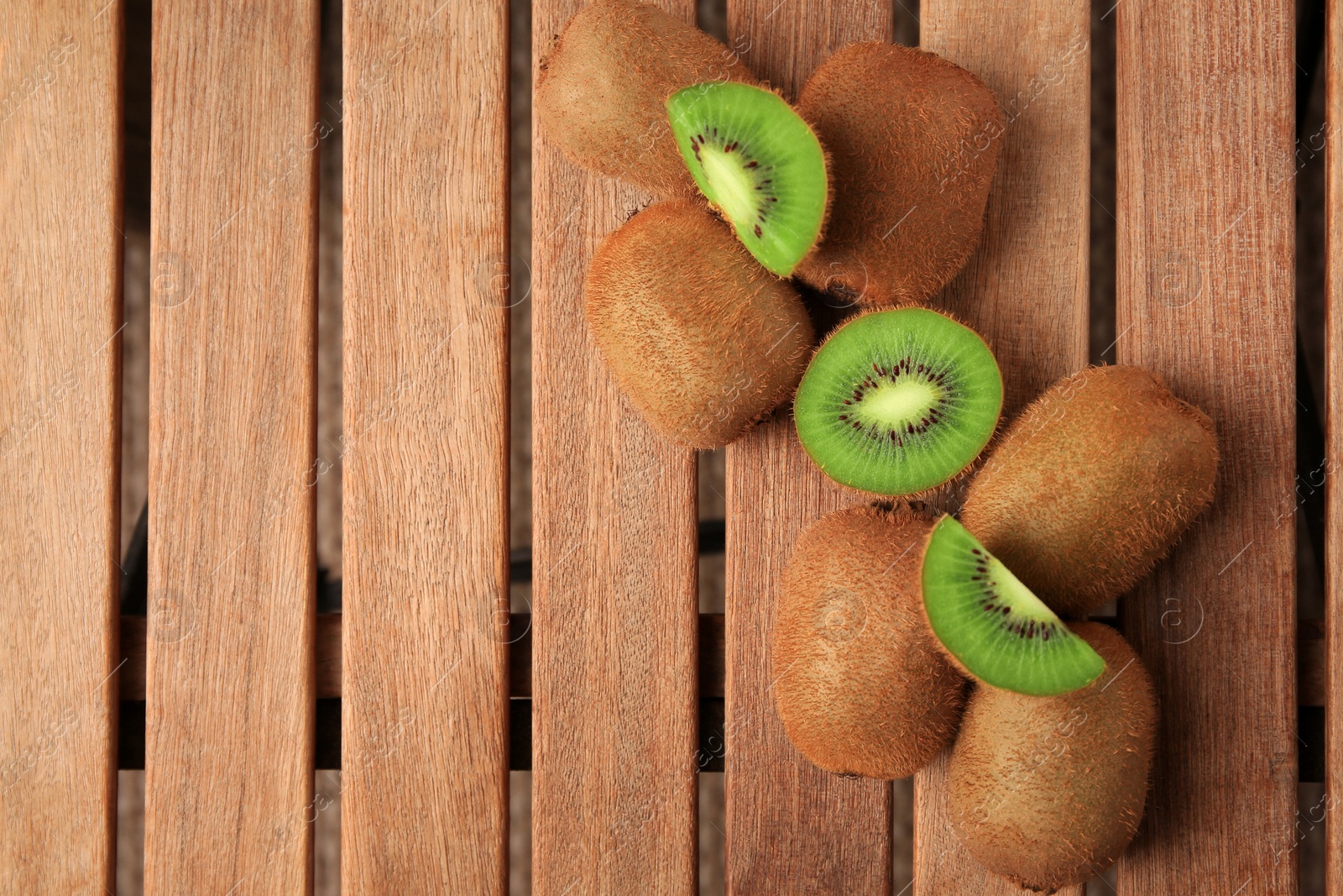 Photo of Whole and cut kiwis on wooden table, flat lay. Space for text