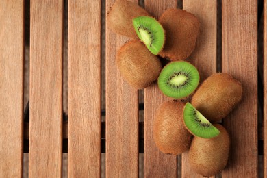 Whole and cut kiwis on wooden table, flat lay. Space for text