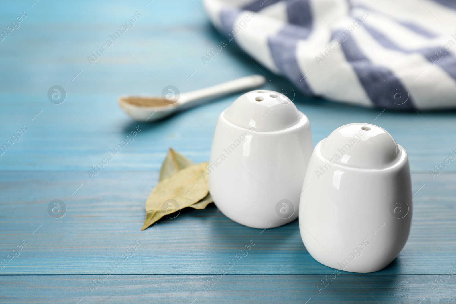 Photo of White ceramic salt and pepper shakers with bay leaves on turquoise wooden table, space for text