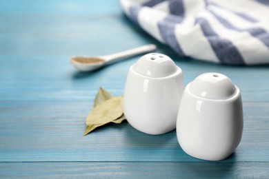 White ceramic salt and pepper shakers with bay leaves on turquoise wooden table, space for text