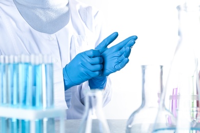 Scientist putting on protective gloves in chemistry laboratory, closeup