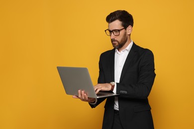 Photo of Bearded man with glasses working on laptop against orange background